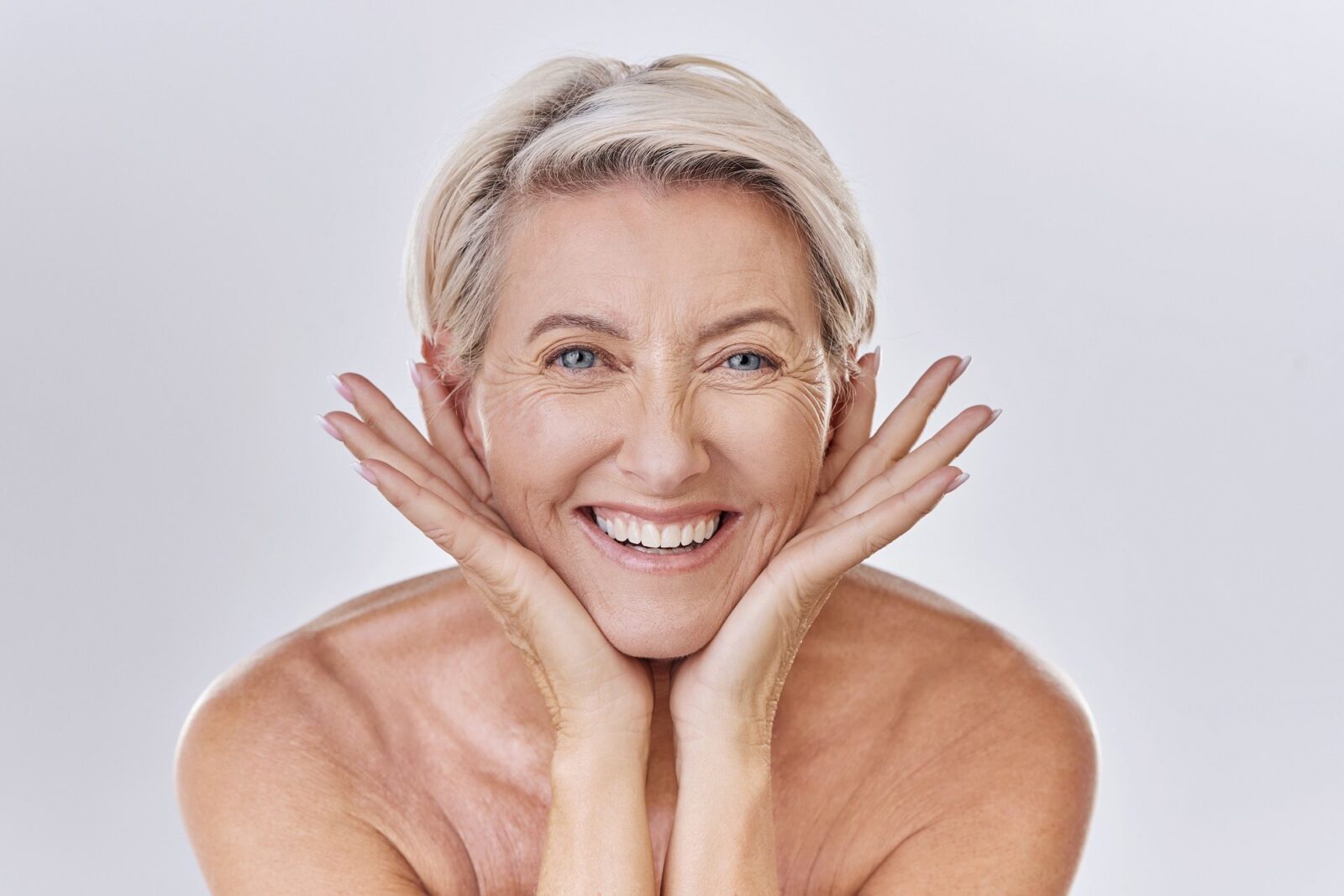 Portrait of a happy smiling mature caucasian woman looking positive and cheerful while caring for her skin in a studio against purple copyspace background. Older woman doing her skincare routine